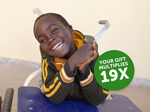 Gerald sitting in a wheelchair smiling. Overlaid text reads 'your gift multiplies 19 times.'