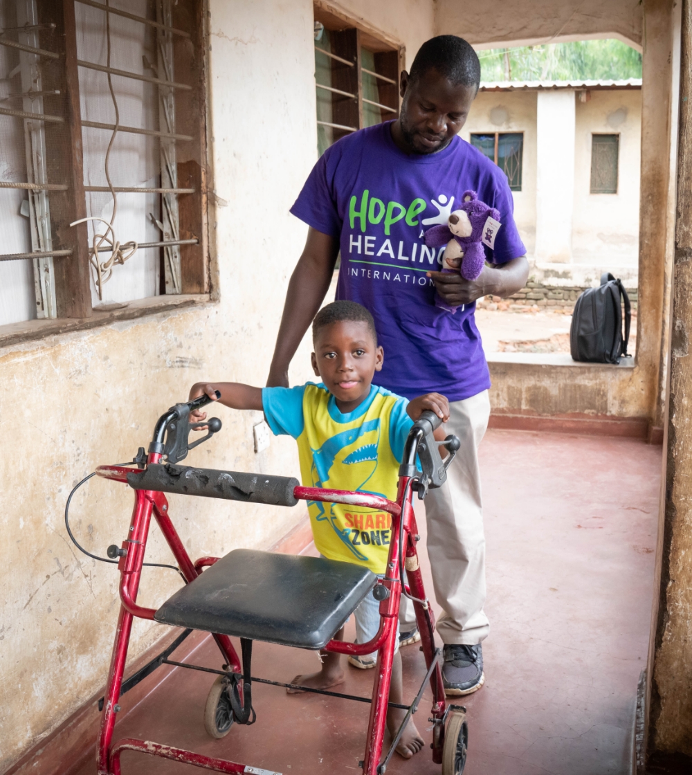 Osman, a young boy with cerebral palsy using his assistive device to walk with the help of a rehabilitation worker.