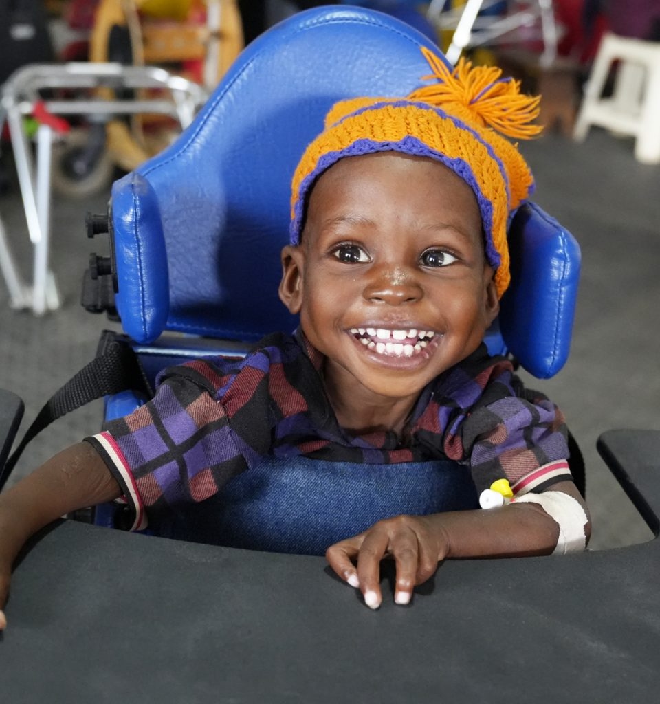 Child wearing a hat and sitting in a wheelchair smiling
