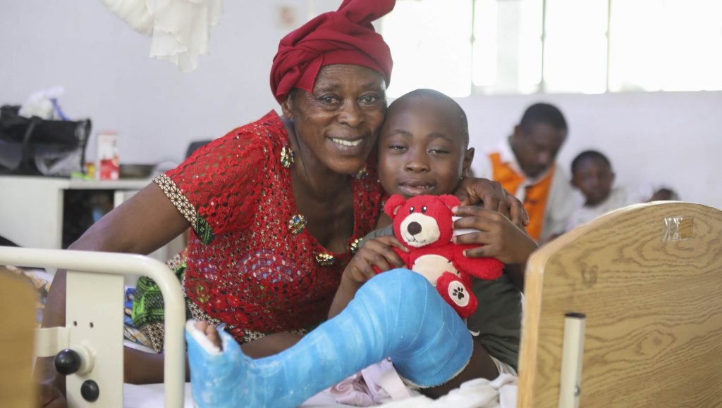 Smiling grandmother with her grandson who is wearing a blue leg cast and holding a red bear.