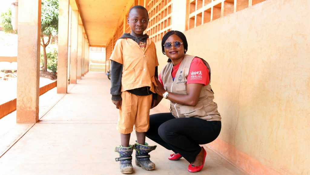 Boy standing on straight feet next to Hope and Healing field worker.