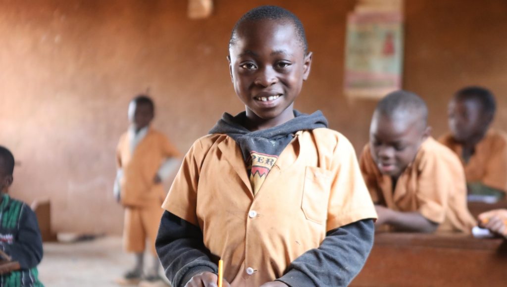 Smiling boy in classroom holding pencil.