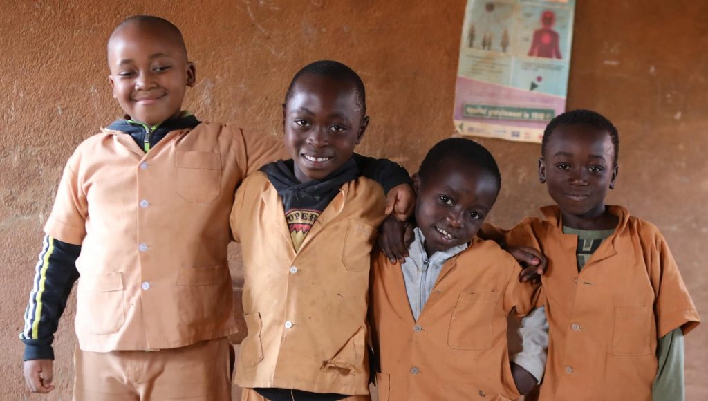 Four boys smiling in school uniforms with arms around each other.