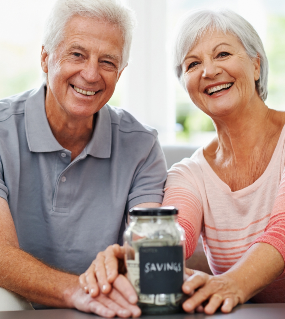 A smiling senior couple holding a savings jar filled with money.