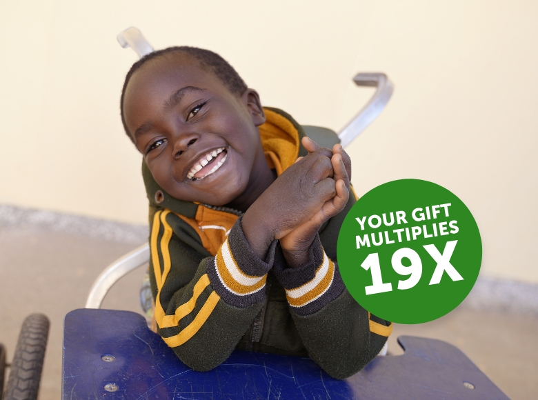 Gerald sitting in a wheelchair smiling. Overlaid text reads "your gift multiplies 19 times."